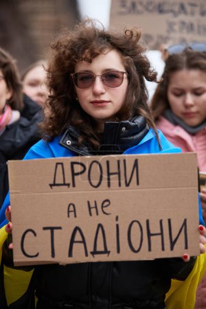 Photo for Ukrainian activist posing with a banner "Drones, Not Stadiums" at a rally for increase of military budget. Kyiv - 23 March,2024 - Royalty Free Image