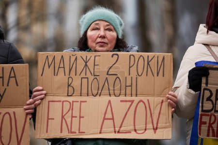 Foto de Triste mujer ucraniana posando con una pancarta "Casi 2 años en prisión. Azov libre "en un mitin para la liberación de los defensores capturados de la ciudad de Mariupol. Kiev - 4 de febrero de 2024 - Imagen libre de derechos