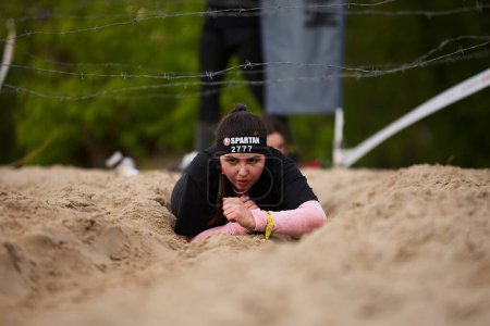 Photo for Young female crawling in the sand under the barbed wire during Spartan Race challenge. Kyiv - 20 April,2024 - Royalty Free Image