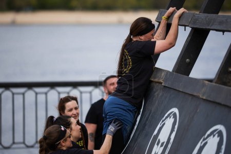Photo for Women help each other to climb the A-shaped wall in a "stairway to sparta" discipline at the Spartan Race competition in Kyiv - 20 April,2024 - Royalty Free Image