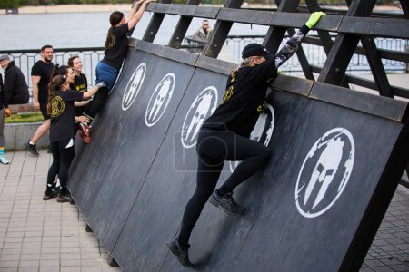 Foto de Mujeres subiendo a la pared de madera en forma de A en una disciplina de "escalera a la esparta" en la competencia de la Spartan Race en Kiev - 20 de abril de 2024 - Imagen libre de derechos