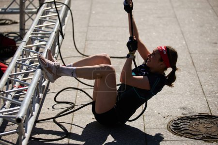 Foto de Joven hembra tira de la cuerda con peso pesado en un polipasto de Hércules en la competición Spartan Race en Kiev - 20 de abril de 2024 - Imagen libre de derechos