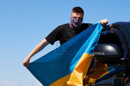 Foto de Patriota ucraniano monta en un coche con una bandera nacional en las manos. Kiev - 28 de abril de 2024 - Imagen libre de derechos