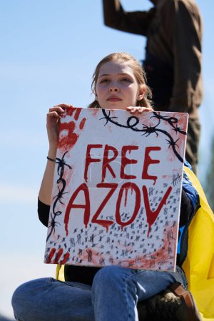 Photo for Young Ukrainian girl sitting with a sing "Free Azov" on a public demonstration. Kyiv - 28 April,2024 - Royalty Free Image