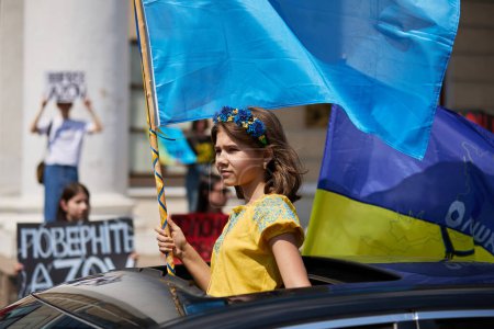 Photo for Young Ukrainian girl rides in a car with a national flag in hand. Kyiv - 19 May,2024 - Royalty Free Image