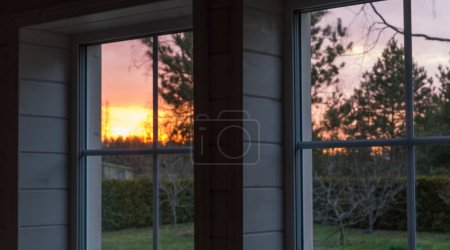 Téléchargez les photos : Belle vue de la fenêtre sur le jardin et la cour dans les rayons du soleil couchant, coucher de soleil. Profondeur de champ faible - en image libre de droit