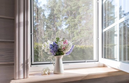 Weißes Fenster mit Moskitonetz in einem rustikalen Holzhaus mit Blick auf den Garten, Kiefernwald. Frühlingsstrauß von Hyazinthen auf der Fensterbank