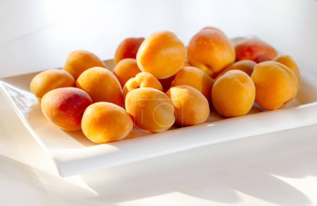 Fresh organic apricot fruit on a white plate and white table. Clean eating concept. Healthy nutritious vegan snack, delicious raw diet.