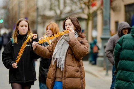 Foto de VILNIUS, LITHUANIA - MARCH 4, 2022: Cheerful young women eating fried potato on a stick on cold winter day outdoors. Having fun with friends. - Imagen libre de derechos