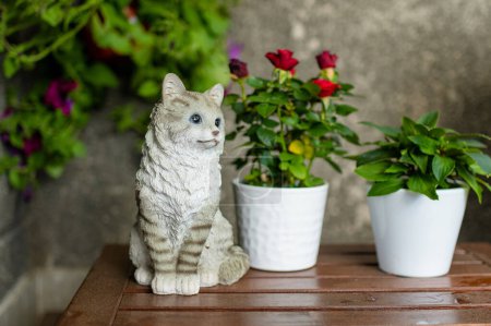 Photo for Plastic cat statue used as a decoration of small outdoor coffee table in the garden. Flower pots and kitty sculture on wooden table. - Royalty Free Image