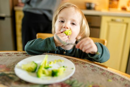 Photo for Cute little toddler boy eating broccoli. First solid foods. Fresh organic vegetables for infants. Healthy nutrition for family with kids. - Royalty Free Image
