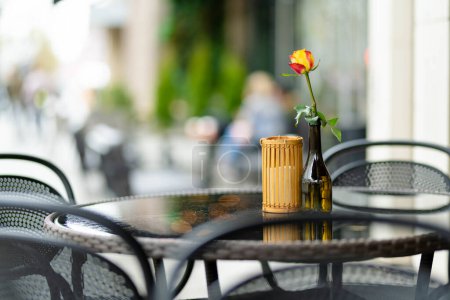 Photo for Outdoor restaurant table beautifully decorated with rose flower in a bottle in Vilnius, Lithuania, on nice summer day. Dining outdoors. - Royalty Free Image