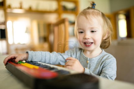 Foto de Divertido niño tocando el piano de juguete en casa. Un niño aprendiendo a tocar el piano. Niño escuchando música. Desarrollo temprano para niños pequeños. Educación musical para niños. - Imagen libre de derechos