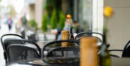Photo for Outdoor restaurant table beautifully decorated with rose flower in a bottle in Vilnius, Lithuania, on nice summer day. Dining outdoors. - Royalty Free Image