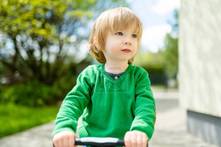 Téléchargez les photos : Petit garçon drôle chevauchant un scooter bébé à l'extérieur le jour de l'été. Équilibre d'entraînement des enfants sur mini vélo dans une cour arrière. Activités estivales pour les petits enfants. - en image libre de droit