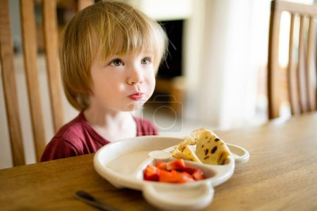 Foto de Lindo niño pequeño comiendo panqueques y fresas en casa. Frescos frutis orgánicos para bebés. Nutrición saludable para la familia con niños. - Imagen libre de derechos