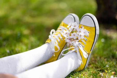 Photo for Female feet in bright yellow sneakers on green grass. Sitting in city park on sunny summer day. Outdoor leisure. - Royalty Free Image