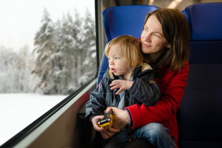 Photo for Young mother and her toddler son traveling by train. Mom and little child sitting by the window in express train on family vacation. Family in a railroad car. Going on vacation with small kids. - Royalty Free Image