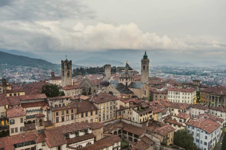 Photo for Scenic aerial view of Bergamo city northeast of Milan, on cloudy evening. Flying over Citta Alta, town's upper district encircled by Venetian walls. Bergamo, Lombardy, Italy. - Royalty Free Image