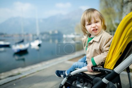 Téléchargez les photos : Petit garçon drôle assis dans une poussette dans la ville de Lecco. Petit enfant en landau. Des promenades en ville avec des enfants. Voyager en Italie avec un petit enfant. - en image libre de droit