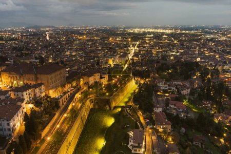 Foto de Vista aérea panorámica de la ciudad de Bérgamo al noreste de Milán, en la noche nublada. Sobrevolando Citta Alta, el distrito superior de la ciudad rodeado de murallas venecianas. Bérgamo, Lombardía, Italia. - Imagen libre de derechos