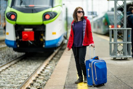 Foto de Una joven en una estación de tren. Una chica esperando un tren en un andén. Turista femenina con maleta de equipaje lista para viajar. Ir de vacaciones solo. - Imagen libre de derechos