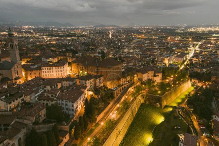 Foto de Vista aérea panorámica de la ciudad de Bérgamo al noreste de Milán, en la noche nublada. Sobrevolando Citta Alta, el distrito superior de la ciudad rodeado de murallas venecianas. Bérgamo, Lombardía, Italia. - Imagen libre de derechos