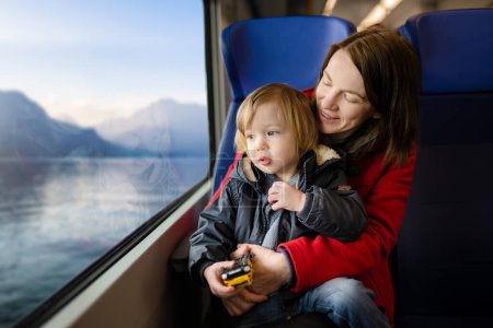 Photo for Young mother and her toddler son traveling by train. Mom and little child sitting by the window in express train on family vacation. Family in a railroad car. Going on vacation with small kids. - Royalty Free Image