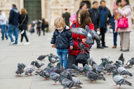 Photo for Young mother and her toddler son feeding the pigeons on the Cathedral Square or Piazza del Duomo in the center of Milan, Lombardy, Italy. - Royalty Free Image