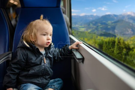 Téléchargez les photos : Petit garçon voyageant en train. Petit enfant assis par la fenêtre en train express en vacances en famille. Enfant dans une voiture de chemin de fer. Partir en vacances avec de jeunes enfants. - en image libre de droit