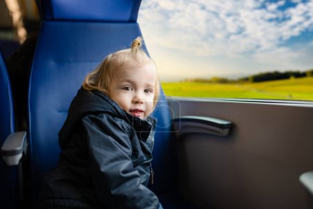 Photo for Toddler boy traveling by train. Little child sitting by the window in express train on family vacation. Kid in a railroad car. Going on vacation with small kids. - Royalty Free Image