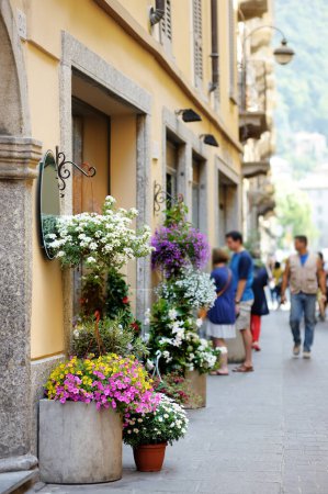 Photo for Variuos flowers blossoming in flower pots on old cobblestone street with souvenir shops, restaurants and cafes in Como town, Lake Como, Italy, Europe - Royalty Free Image