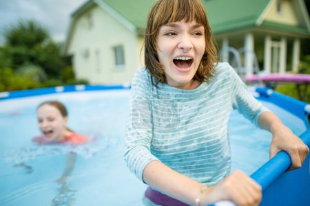 Téléchargez les photos : Deux sœurs adolescentes drôles essayant d'entrer dans l'eau froide de la piscine. Les enfants s'amusent dans la piscine extérieure. Amusement en famille dans une piscine. Activités estivales pour la famille avec enfants. - en image libre de droit