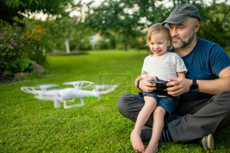 Téléchargez les photos : Père et fils regardent et naviguent dans un drone. Petit garçon mignon aidant son père à faire fonctionner un drone par télécommande. Loisirs en famille. - en image libre de droit