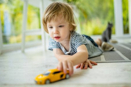 Photo for Cute toddler boy playing with yellow toy car. Small child having fun with toys. Kid spending time in a cozy living room at home. Family leisure indoors. - Royalty Free Image