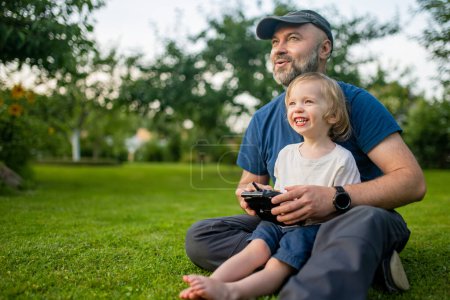 Photo for Father and son watching and navigating a drone. Cute toddler boy helping his father to operate a drone by remote control. Family leisure. - Royalty Free Image