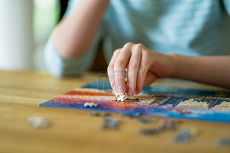 Photo for Close-up on woman hand playing puzzles at home. Connecting jigsaw puzzle pieces in a living room table, assembling a jigsaw puzzle. Fun family leisure. - Royalty Free Image