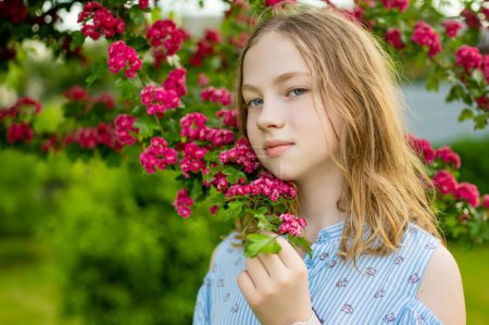 Téléchargez les photos : Beau portrait d'adolescente en fleurs d'aubépine rose décoratives sur le buisson. Plante d'aubépine en fleurs dans le jardin de printemps. Beauté dans la nature. - en image libre de droit