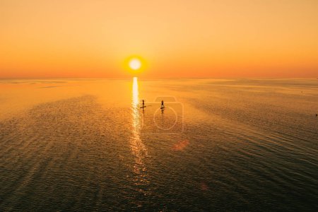 Photo for Aerial view of two people on stand up paddle boards on quiet sea at sunset. Warm summer beach vacation holiday. Active leisure on a seaside. - Royalty Free Image