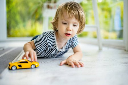 Téléchargez les photos : Bébé mignon garçon jouant avec voiture jouet jaune. Petit enfant s'amuser avec des jouets. Le gamin passe du temps dans un salon confortable à la maison. Loisirs familiaux à l'intérieur. - en image libre de droit