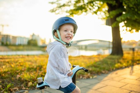 Foto de Divertido niño montado en un bebé scooter al aire libre en el día de verano. Equilibrio de entrenamiento para niños en mini bicicleta. Actividades de verano para niños pequeños. - Imagen libre de derechos