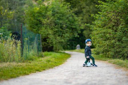 Foto de Divertido niño montado en un bebé scooter al aire libre en el día de otoño. Equilibrio de entrenamiento infantil en mini bicicleta en un parque de la ciudad. Niño explorando la naturaleza. Actividades de otoño para niños pequeños. - Imagen libre de derechos
