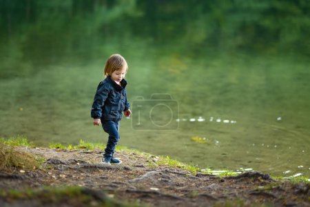 Foto de Adorable niño admirando el lago Balsys, uno de los seis Lagos Verdes, ubicado en el Parque Regional de Verkiai. Niño explorando la naturaleza en el día de otoño en Vilna, Lituania. Actividades divertidas de otoño para niños. - Imagen libre de derechos