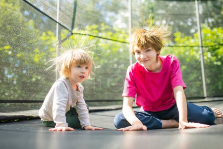 Photo for Cute toddler boy and his sister jumping on a trampoline in a backyard. Sports and exercises for children. Summer outdoor leisure activities. - Royalty Free Image