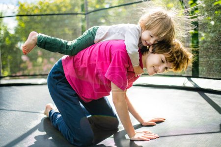 Téléchargez les photos : Mignon tout-petit garçon et sa sœur sautant sur un trampoline dans un jardin. Sports et exercices pour les enfants. Activités de plein air estivales. - en image libre de droit