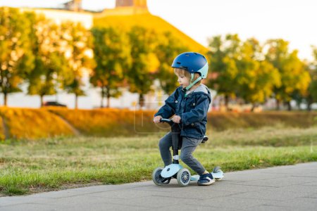 Foto de Divertido niño montado en un bebé scooter al aire libre en el día de otoño. Equilibrio de entrenamiento infantil en mini bicicleta en un parque de la ciudad. Niño explorando la naturaleza. Actividades de otoño para niños pequeños. - Imagen libre de derechos