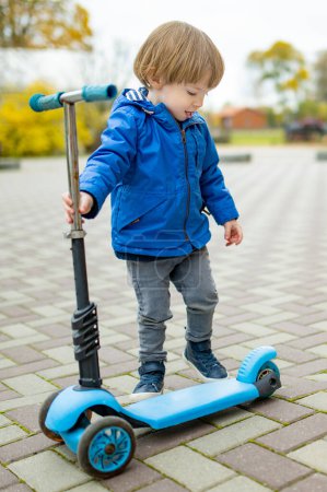 Photo for Adorable toddler boy riding his scooter in a city on sunny autumn evening. Young child riding a roller. Active leisure and outdoor sports for kids. - Royalty Free Image