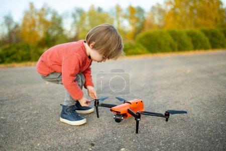 Téléchargez les photos : Joli gamin qui regarde un drone. Petit garçon mignon aidant son père à faire fonctionner un drone par télécommande. Loisirs en famille. - en image libre de droit