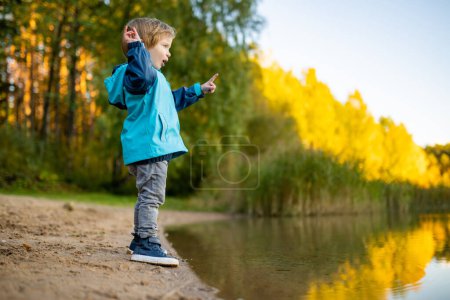 Foto de Adorable niño divirtiéndose junto al lago Gela en el soleado día de otoño. Niño explorando la naturaleza en el día de otoño en Vilna, Lituania. Actividades divertidas de otoño para niños. - Imagen libre de derechos