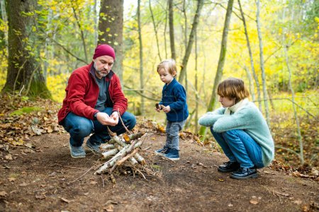 Photo for Father and children roasting marshmallows on sticks at bonfire. Children having fun at camp fire. Camping with kids in fall forest. Family leisure with kids at autumn. - Royalty Free Image